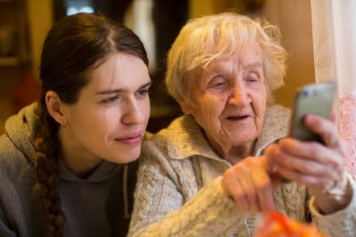 an elderly old woman looks at a smartphone with her adult granddaughter