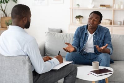 stressed african man explaining his problems to psychologist at individual therapy session