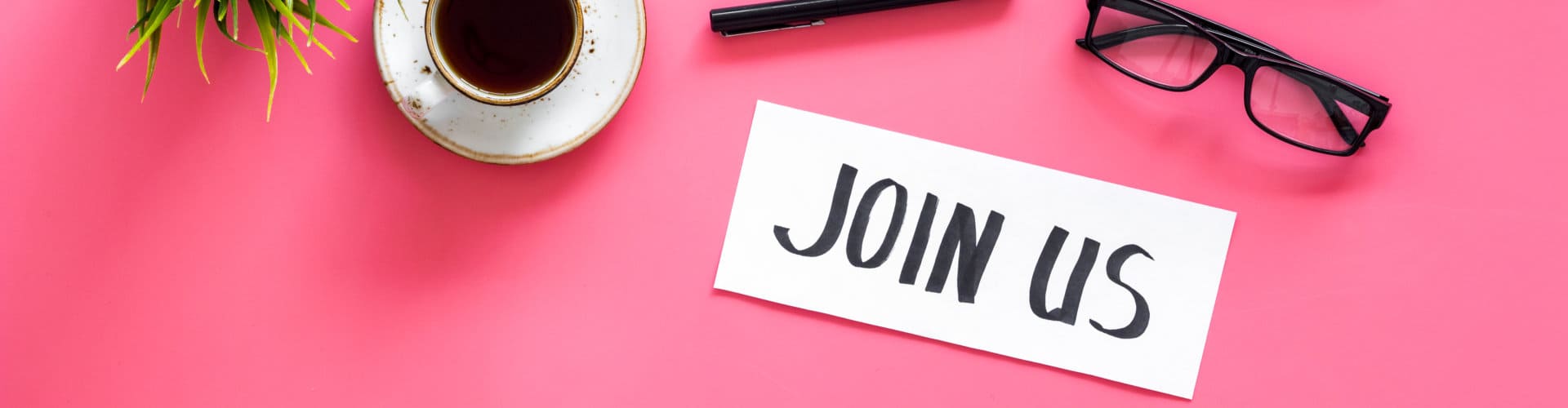 Hand lettering Join us on work desk with glasses, coffe, plant, computer keyboard on pink background