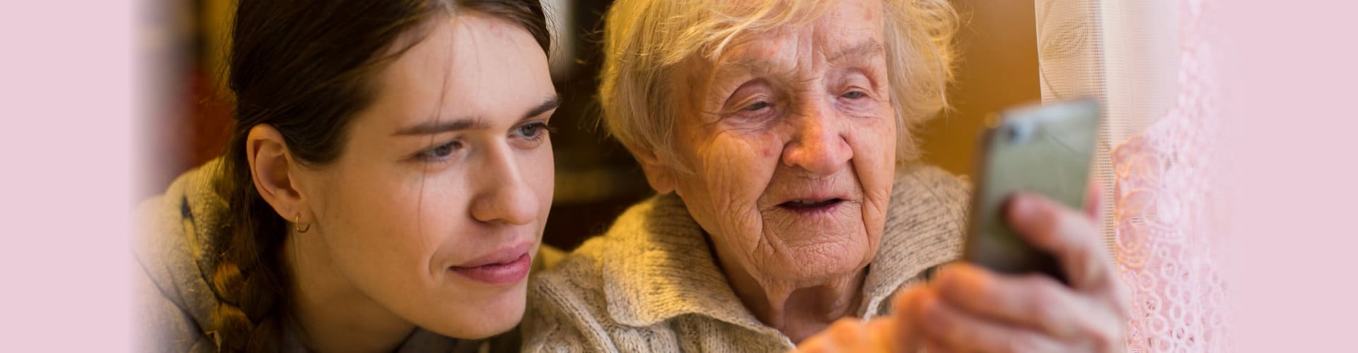 an elderly old woman looks at a smartphone with her adult granddaughter